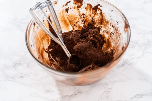 Scooping cookie dough with dough scoop into a baking sheet lined with parchment paper to bake chocolate cookies with chocolate hearts for Valentine's Day.