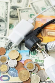 The concept of the energy crisis, price increases. Euro and dollar banknotes, coins on the background of a lamp, plug, cord. Tax time, bill payment, calculator for counting. Vertical photo