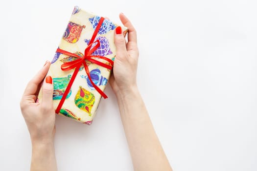 The girl holds a gift in her hands with a red ribbon and multi-colored paper on a white background. Time to wrap presents. Surprise, Christmas and New Year concept