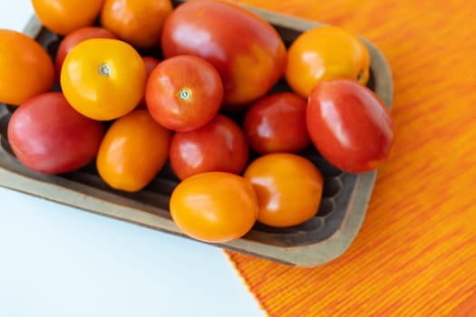 Fresh bright multi-colored red-yellow tomatoes in a wooden plate on the table. View from above