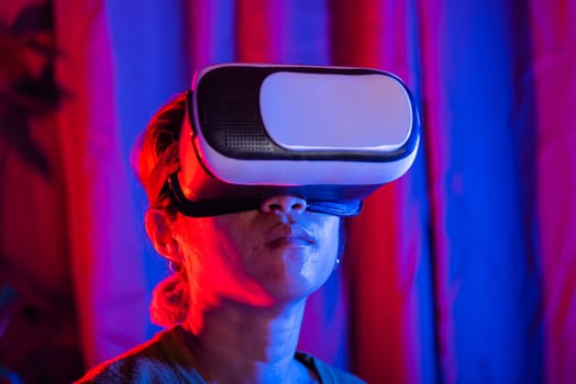 Asian woman wear the VR helmet excited emotional at home purple and blue background, female experiencing virtual reality goggles experiencing reality, metaverse and cyberspace concept