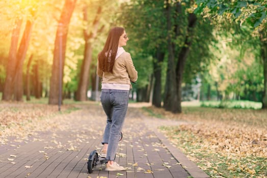 Young woman riding an electric scooter in autumn park. Green transport, traffic jam problems.