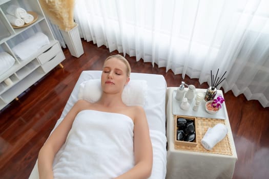 Caucasian woman customer enjoying relaxing anti-stress spa massage and pampering with beauty skin recreation leisure in day light ambient salon spa at luxury resort or hotel. Quiescent