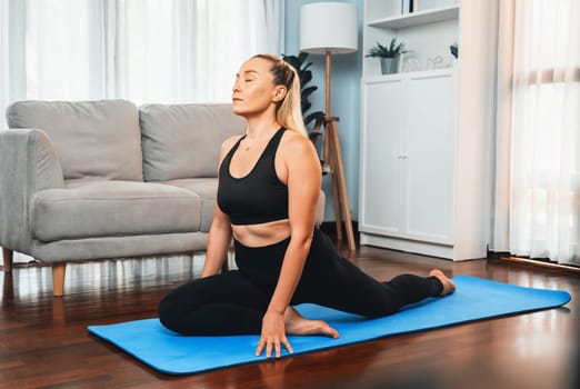 Senior woman in sportswear being doing yoga in meditation posture on exercising mat at home. Healthy senior pensioner lifestyle with peaceful mind and serenity. Clout