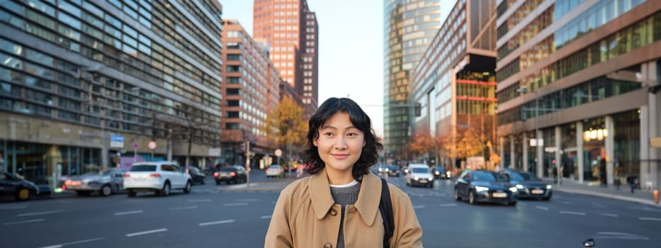 Portrait of smiling korean girl stands on busy street of city centre, holds digital tablet, casual relaxed face expression, walking around town.