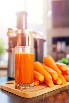 Glass of freshly squeezed carrot juice, carrots and juicer in the kitchen. Healthy lifestyle concept