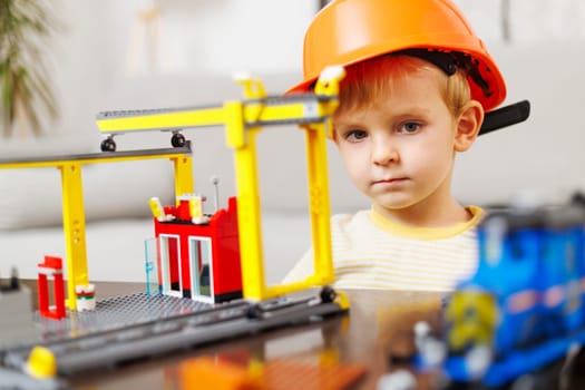 Child boy in helmet playing and building with colorful plastic bricks at the table. Early learning and development