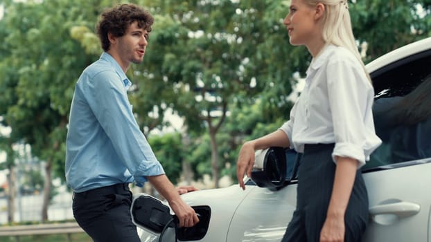 Progressive businessman and businesswoman install charger plug from charging station to electric car before driving around city center. Eco friendly rechargeable car powered by clean energy.