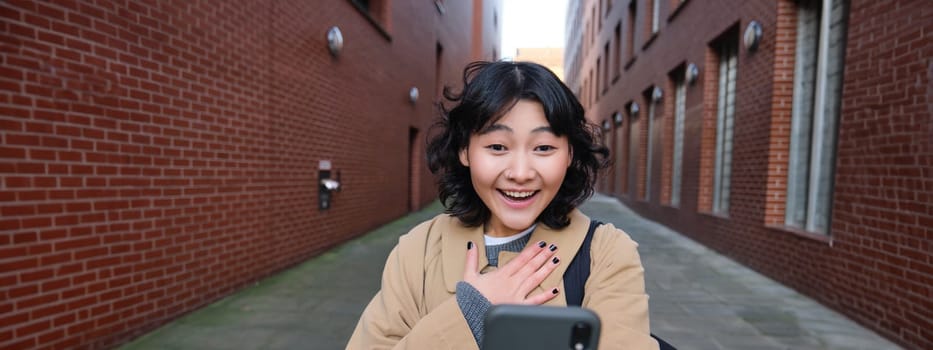 Portrait of amazed girl, looks at smartphone screen and gasps from happiness, reads good news on text message, being impressed by smth on mobile phone.