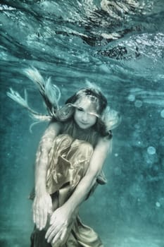Young beautiful woman in golden dress underwater