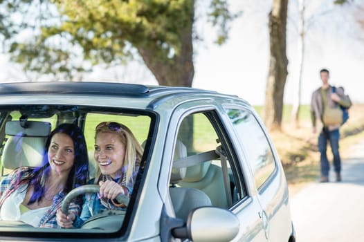 Two women happy in car taking handsome hitch-hiker road trip