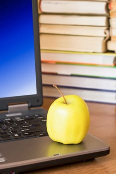 laptop with yellow apple on books background