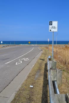 On a rural road in Stoney Creek, Ontario, a sign and markings on the street shows this is a designated lain for bicycles, background lake Ontario.