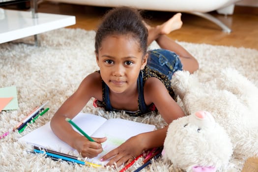 Little African Asian girl  drawing, lying down on the floor