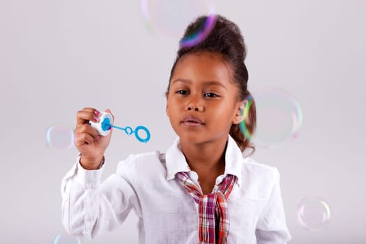 Cute little African American girl blowing soap bubbles