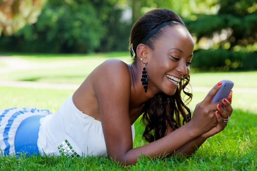 Smiling teenage black girl using a phone, lying on the grass