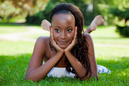 Thoughtful young african american girl lying down on the grass