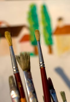 Paintbrushes and painted canvas in the background