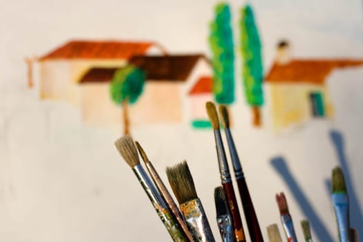 Paintbrushes and painted canvas in the background