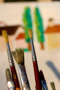 Paintbrushes and painted canvas in the background