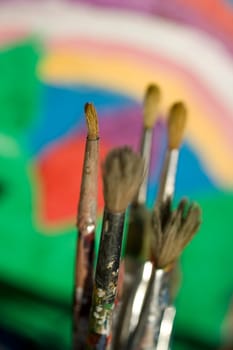 Paintbrushes and painted canvas in the background