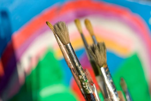 Paintbrushes and painted canvas in the background