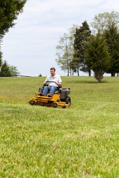 Senior retired male cutting the grass on expansive lawn using yellow zero-turn mower