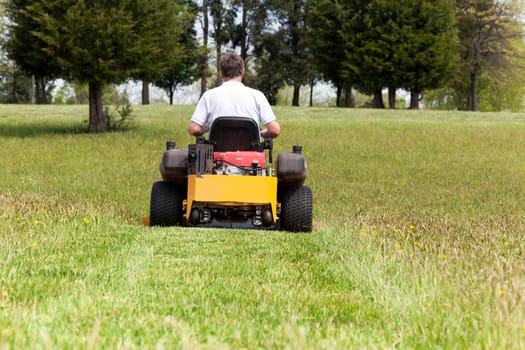 Senior retired male cutting the grass on expansive lawn using yellow zero-turn mower