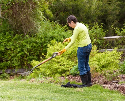 Woman gardener tosses away garden fork in frustration when weeding flowerbed