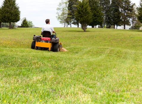 Senior retired male cutting the grass on expansive lawn using yellow zero-turn mower