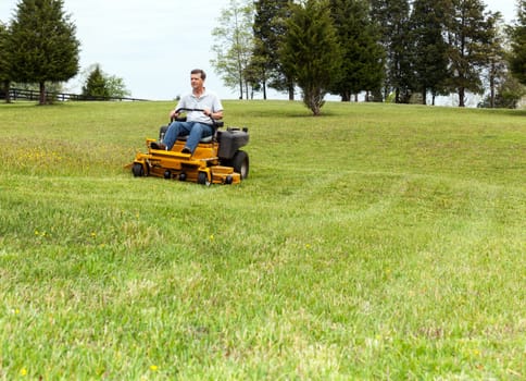Senior retired male cutting the grass on expansive lawn using yellow zero-turn mower