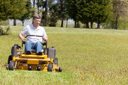 Senior retired male cutting the grass on expansive lawn using yellow zero-turn mower