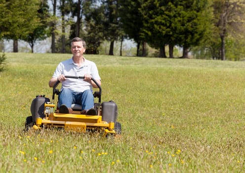 Senior retired male cutting the grass on expansive lawn using yellow zero-turn mower