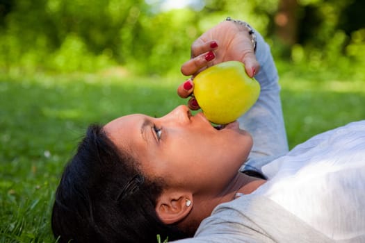 Beautiful black woman laying down outside on grass  eating an apple