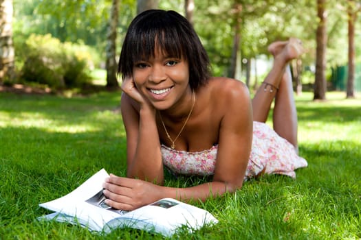 Outdoor portrait of young african american woman lying down on the grass reading a book