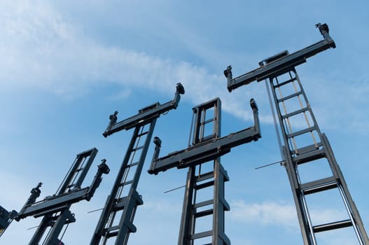 several forklifts for containers against a blue sky