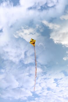 a smiley kite high in the cloudy blue sky