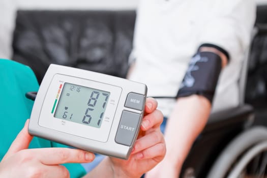 Young man having blood pressure check at home. He is in wheelchair.