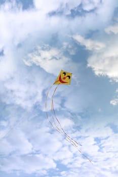 a smiley kite high in the cloudy blue sky
