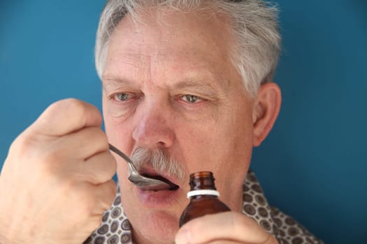 a senior takes a spoonful of cough syrup