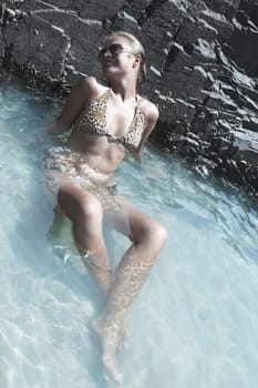 Beautiful woman sitting in water near the rock