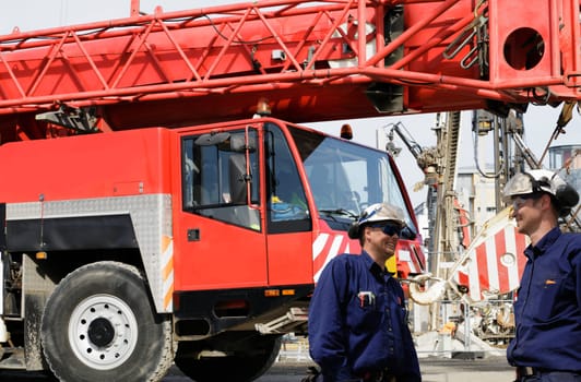 two building-workers with giant red mobile crane in background