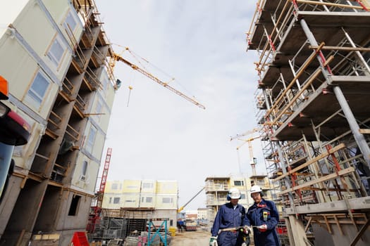 two building-workers surrounded by giant building site, cranes and scaffolding