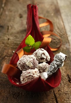 Chocolates in a red palm bowl, luxury ambient. For Truffle and Chocolate concepts. On a wooden Background.