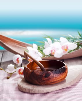 Ethnic luxurious spa treatment with a simply crafted bowl of natural wood laid out in front of exotic orchids against an idyllic ocean backdrop