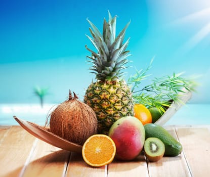 Fresh Fruits on the beach at a deck in front of an island with a palm. Assorted tropical fruits, orange,Ananas or pineapple, lime,mango and avocado.
