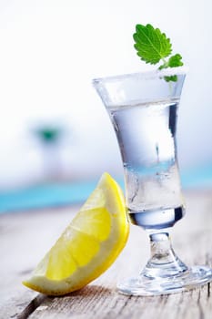 Cold vodka in a frosted shot glass served with lemon chaser alongside a blue pool in summer