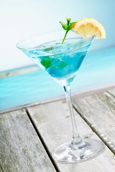 Refreshing classical blue curacao martini cocktail garnished with fresh lemon and served alongside the ocean on a tropical vacation