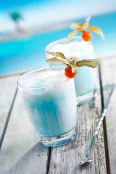 Two glasses of blended blue cold curacao cocktail on a deck overlooking the sea at a tropical resort