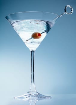 Shaken martini cocktail in a conical glass with an olive on a suffused soft blue background